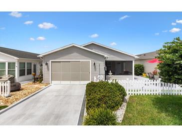 Charming single-story home with gray siding, a well-maintained lawn, a white picket fence, and a convenient attached garage at 1513 Lozano Ave, The Villages, FL 32159