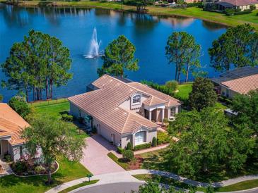 Beautiful lakefront home featuring lush landscaping, tile roof, and brick driveway with a scenic fountain view at 2029 Stefano Ct, Mount Dora, FL 32757