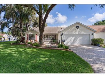 Charming single-story home with a well-maintained lawn, mature trees and brick-paved driveway leading to a two car garage at 411 Loma Paseo Dr, The Villages, FL 32159
