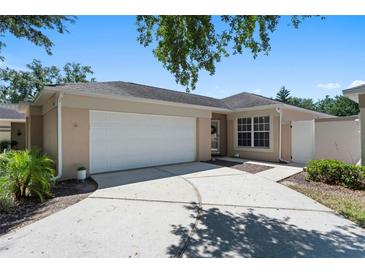 Well-maintained, light-colored home with a two-car garage and concrete driveway nestled under mature trees on a sunny day at 2012 Braxton St, Clermont, FL 34711