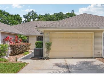 Beige two car garage with neutral siding and walkway to the front door surrounded by lush landscaping at 340 Juniper Way, Tavares, FL 32778