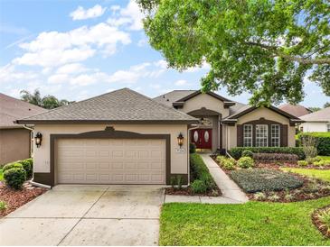 Charming home featuring manicured landscaping, a two-car garage, and a welcoming red double-door entrance at 7034 Pine Hollow Dr, Mount Dora, FL 32757