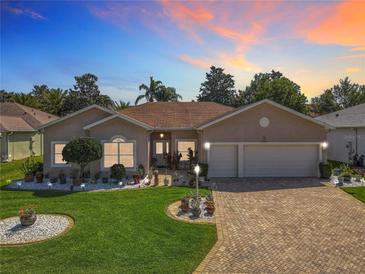 Charming one-story home featuring a brick driveway, a well-manicured lawn, and lovely landscaping at sunset at 24436 Madewood Ave, Leesburg, FL 34748