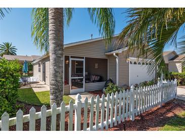 Exterior of a charming home showcasing a screened in porch, white picket fence, and well manicured landscaping at 992 Pinewood Pl, The Villages, FL 32162