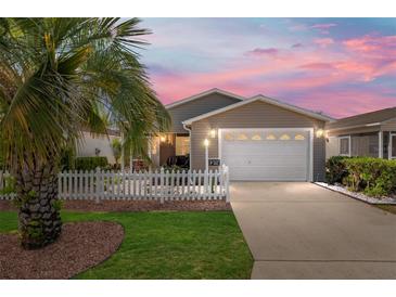 Charming home featuring a white picket fence, well-manicured lawn, and a driveway leading to the garage at 992 Pinewood Pl, The Villages, FL 32162