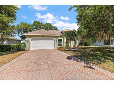 Charming single-story home with a two-car garage and brick-paved driveway, complemented by lush landscaping at 38420 Langlois Pl, Leesburg, FL 34788