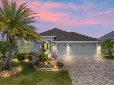 Charming single-story home with a well-manicured lawn, paver driveway, and lush landscaping at twilight at 575 Wheelock St, The Villages, FL 32163