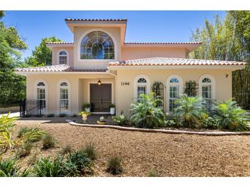 Charming home features a barrel tile roof and arched windows surrounded by lush landscaping and mulch beds at 1196 Lakeshore Dr, Mount Dora, FL 32757