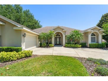 Inviting single-story home featuring a well-manicured lawn, arched entryway, and mature landscaping at 13045 Colonnade Cir, Clermont, FL 34711