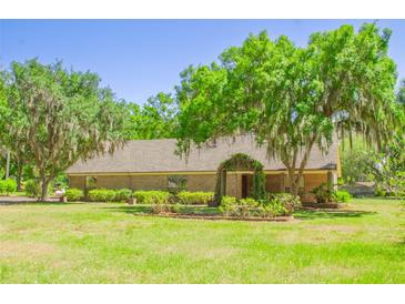 Charming home exterior featuring a well-manicured lawn, mature trees, and a welcoming garden trellis entrance at 2112 Robie Ave, Mount Dora, FL 32757