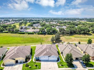 A beautiful home exterior featuring lush green lawns, a golf course, and a light blue sky with fluffy white clouds at 27018 White Plains Way, Leesburg, FL 34748