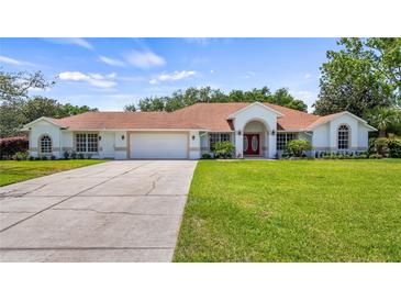 Beautiful single-story home featuring a well-manicured lawn, red double door entrance, and attached two car garage at 17825 Whisperwind Dr, Clermont, FL 34715