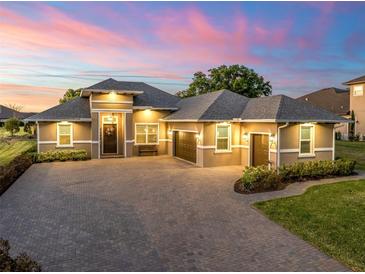 Stunning home exterior boasts lush landscaping, a paver driveway, and a three-car garage beneath a colorful twilight sky at 39653 Grove Hts, Lady Lake, FL 32159