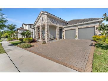 Beautiful home features a two-car garage, brick paved driveway, stone accents, and manicured landscaping at 8272 Procida Isle Ln, Windermere, FL 34786