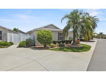 Charming single-story home featuring a well-manicured lawn, lush landscaping, and a mature palm tree at 2293 Wayland St, The Villages, FL 32162