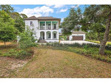 Elegant two-story white home with a charming veranda and lush landscaping on a well-maintained lawn at 6905 Clayton St, Mount Dora, FL 32757