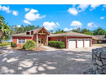 Lovely home featuring a charming red exterior, lush landscaping, and a large driveway at 2400 N Griffin Dr, Leesburg, FL 34748