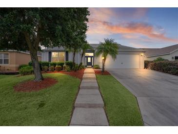 Charming home featuring a manicured lawn, mature trees, and a walkway leading to the front door at 506 Weston Manor Dr, The Villages, FL 32162