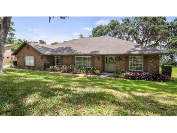 Charming brick home featuring a manicured lawn, mature landscaping, and inviting front entrance with beautiful shutters at 12104 Elbert St, Clermont, FL 34711