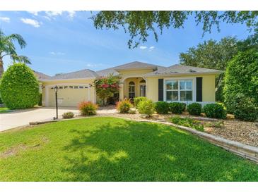 Charming yellow home with lush green lawn, lovely landscaping, and a two-car garage at 1446 Arbor Trl, The Villages, FL 32162