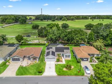 Beautiful aerial view of a home featuring well-maintained landscaping, solar panels, and a lovely green field in the background at 3534 Auburndale Ave, The Villages, FL 32162