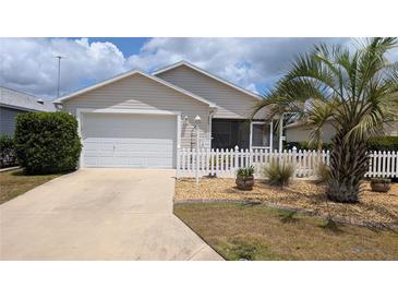 Charming home featuring a well-maintained lawn, a white picket fence, and a two-car garage at 971 Margaux Trl, The Villages, FL 32162