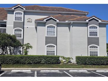 Exterior view of condo building with gray accents, a red tile roof, and well-maintained landscaping in a parking lot at 14049 Fairway Island Dr # 118, Orlando, FL 32837