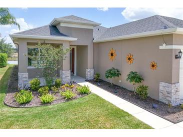 Charming home exterior with a well-manicured lawn, stone accents, and decorative floral accents at 8664 Bridgeport Bay Cir, Mount Dora, FL 32757