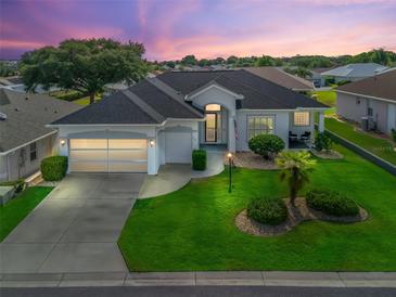 Beautiful single-story home with well-manicured lawn, mature landscaping, and two-car garage under a purple sunset sky at 17471 Se 110Th Ter, Summerfield, FL 34491