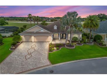 Beautiful single-story home with a three-car garage, a brick driveway, and mature landscaping at sunset at 2954 Cedar Grove Loop, The Villages, FL 32163