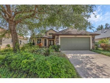 Charming home with lush landscaping and a stone-accented facade and a two-car garage, all shaded by a mature tree at 8167 Bridgeport Bay Cir, Mount Dora, FL 32757