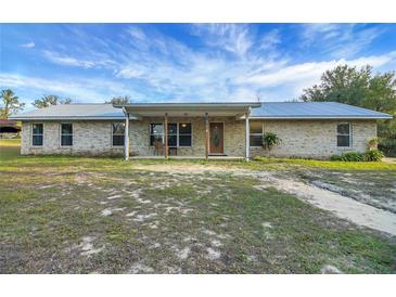 Charming single-story brick home with a metal roof and covered front porch with beautiful blue skies above at 9236 County Road 48, Yalaha, FL 34797