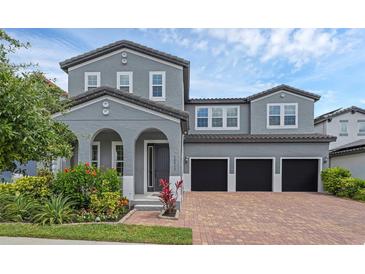 Two-story gray home featuring a brick driveway, a three-car garage, and beautiful landscaping at 14513 Winter Stay Dr, Winter Garden, FL 34787