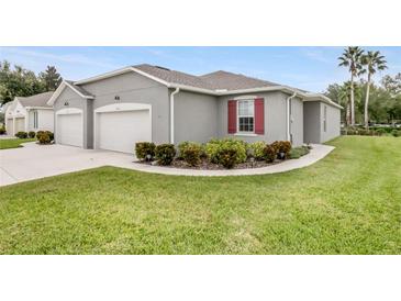 A modern one-story home with a gray exterior, two-car garage, and a well-manicured lawn with shrubbery at 27215 White Plains Way, Leesburg, FL 34748