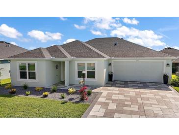 Charming home featuring a manicured lawn, paver driveway, and coordinated landscaping at 1627 Mclucas Ln, The Villages, FL 34762