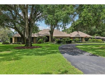 Charming single-story home with mature trees, lush lawn, and a circular driveway providing ample parking space at 1930 Country Club Rd, Eustis, FL 32726