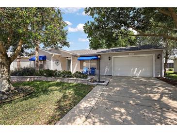 Charming single-story home with an attached garage, blue awnings, and well-maintained landscaping at 2003 Cordero Ct, The Villages, FL 32159