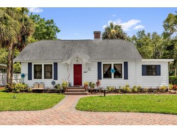 Charming one-story home featuring a brick pathway, vibrant red door, and meticulously landscaped yard at 647 E 3Rd Ave, Mount Dora, FL 32757