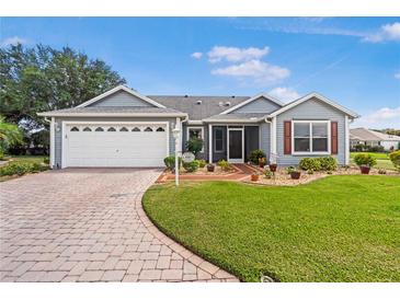 Charming single-story home featuring a manicured lawn, brick driveway, and attached two-car garage at 8980 Se 176Th Limerick Ln, The Villages, FL 32162