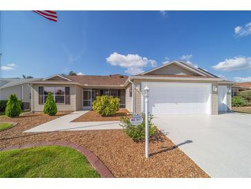 Inviting home with tan siding, manicured lawn, two-car garage, and mature landscaping at 997 Nash Loop, The Villages, FL 32162