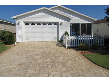 Charming single-story home with a white picket fence, brick driveway, and well-maintained lawn at 2388 Branchville Ter, The Villages, FL 32162