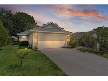A home exterior is seen at dusk with a paved driveway leading to the garage, surrounded by mature landscaping at 2821 Mediterranean Loop, Tavares, FL 32778