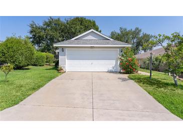 Home featuring a spacious driveway leading to an attached two-car garage and front yard with mature landscaping at 2821 Mediterranean Loop, Tavares, FL 32778
