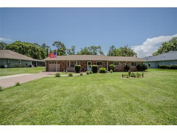 Charming brick home featuring a well-maintained lawn, an American flag, and a brick driveway at 11418 Lake Eustis Dr, Leesburg, FL 34788