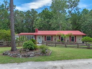 Charming single-story home featuring a red roof, shutters, landscaped front yard and a rustic wooden fence at 12288 Sw 35Th Dr, Webster, FL 33597