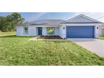 Charming single-story home featuring a blue garage door, grey roof, and nicely landscaped front yard at 472 Malauka Radl, Ocklawaha, FL 32179