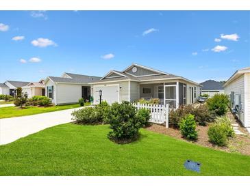 Charming single-story home featuring a well-manicured lawn, white picket fence, and screened porch at 1225 Eunice St, The Villages, FL 34762