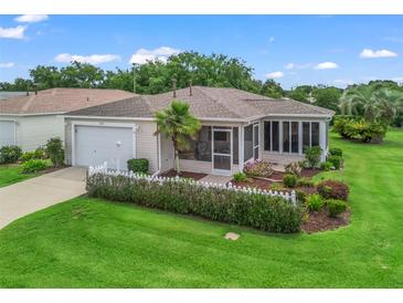 Charming single-story home featuring a well-manicured lawn, white picket fence, and a cozy screened lanai at 17461 Se 82Nd Albemarle Ave, The Villages, FL 32162