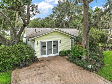 A yellow siding garage featuring carriage doors and brick paving surrounded by manicured shrubbery and mature trees at 24 Brigadoon Cir, Leesburg, FL 34788