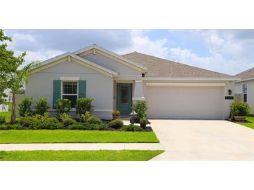 Charming single-story home features a well-manicured lawn, a two-car garage, and a decorative teal front door at 33647 Sky Blossom Cir, Leesburg, FL 34788